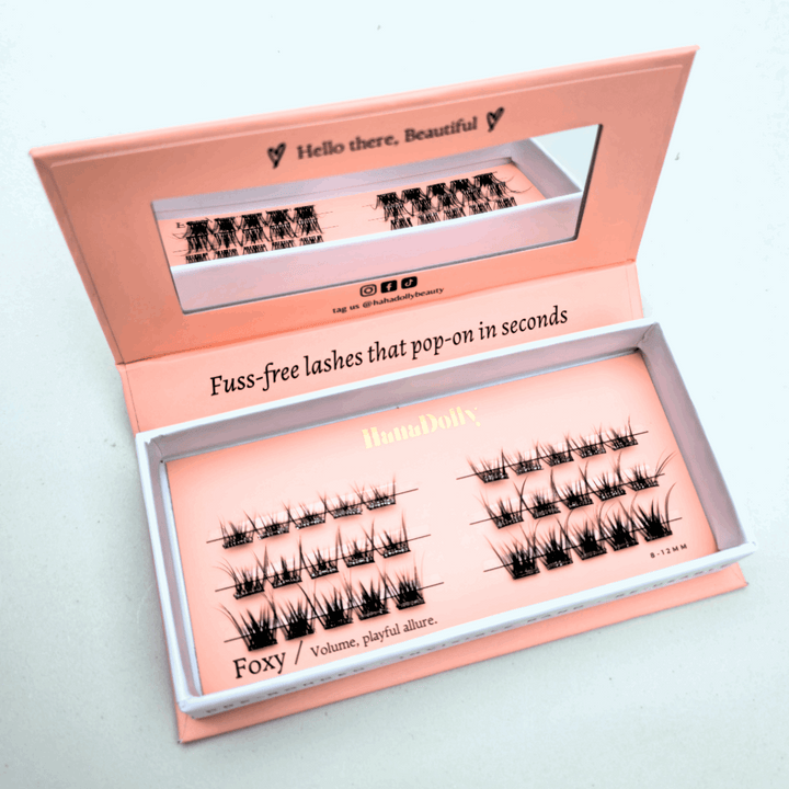 Angled flatlay of HanaDolly FOXY press-on lashes in an open pink box, showing individual lash clusters for easy application.