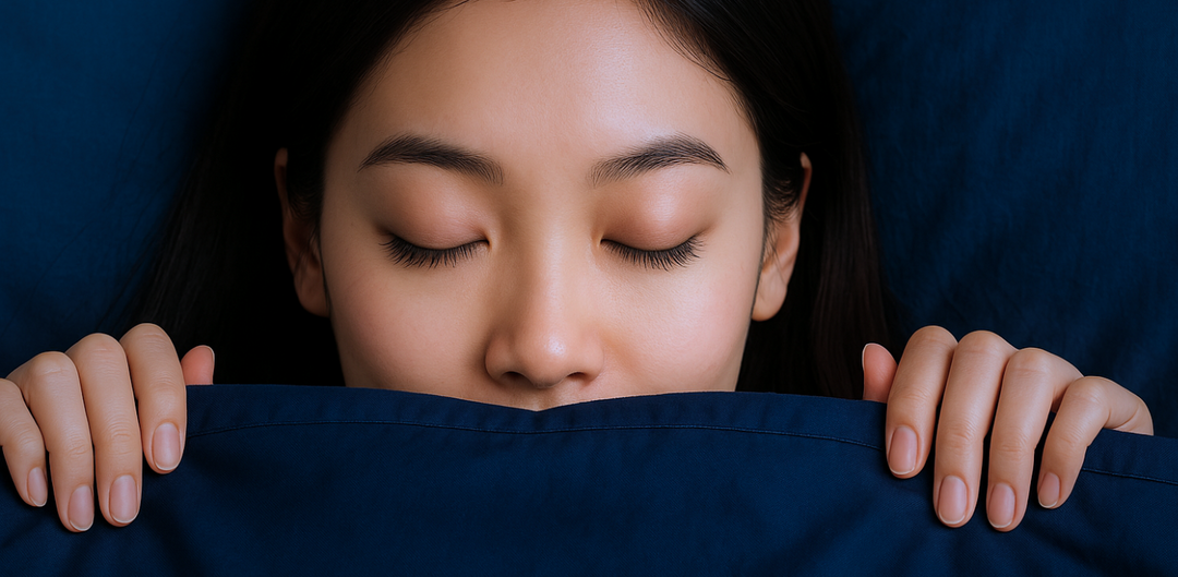 Asian woman sleeping peacefully behind a navy blanket with closed eyes, showing how to sleep safely with DIY eyelash extensions.
