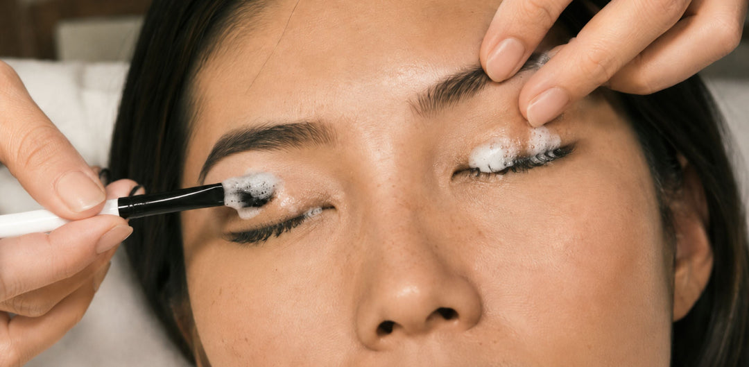 Asian woman cleaning eyelash extensions with lash foam during a professional lash care treatment for better lash hygiene and retention.