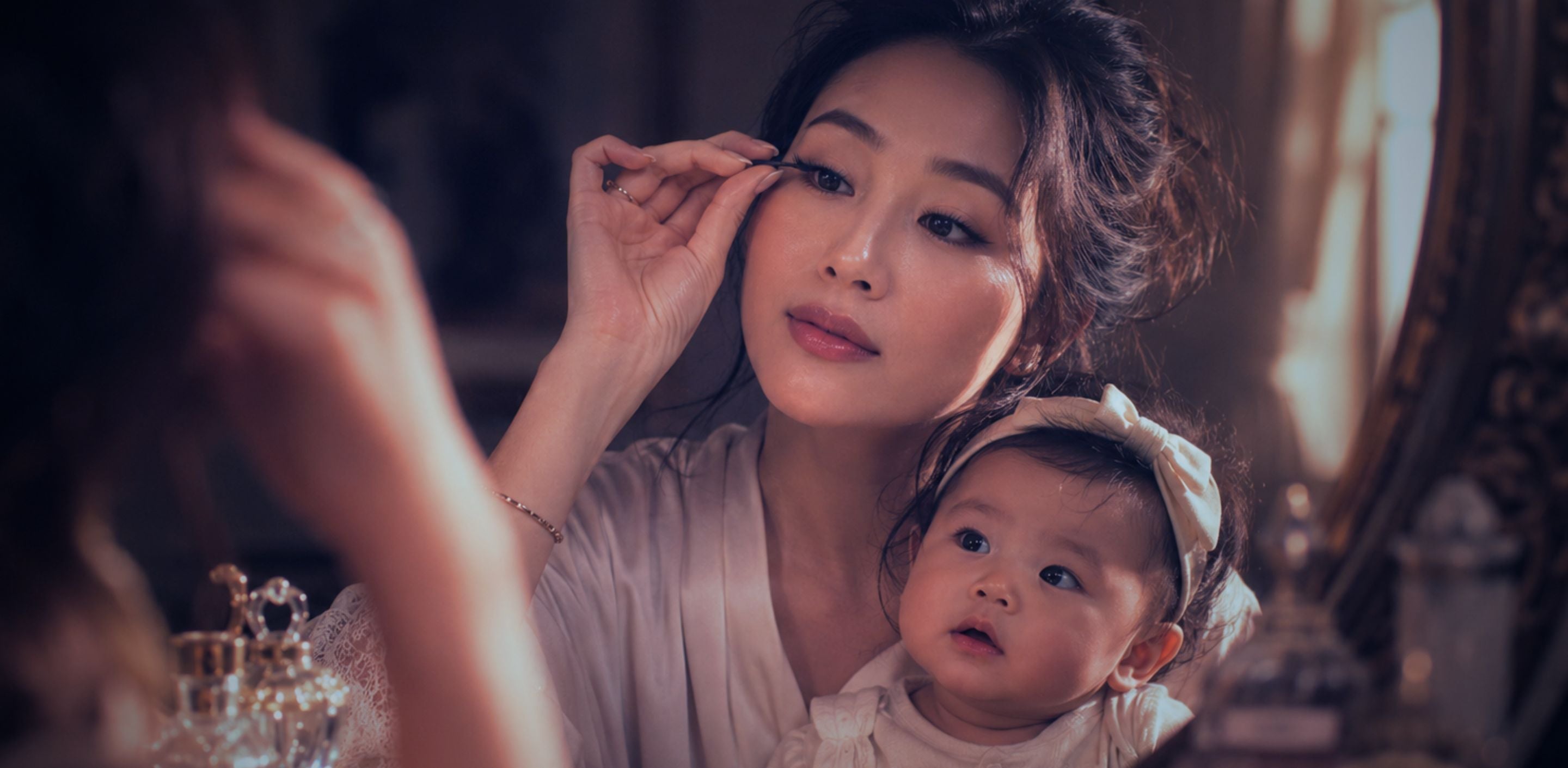 Singaporean mother holding her baby while applying press-on lashes, representing postpartum eyelash loss and gentle lash care for mums.