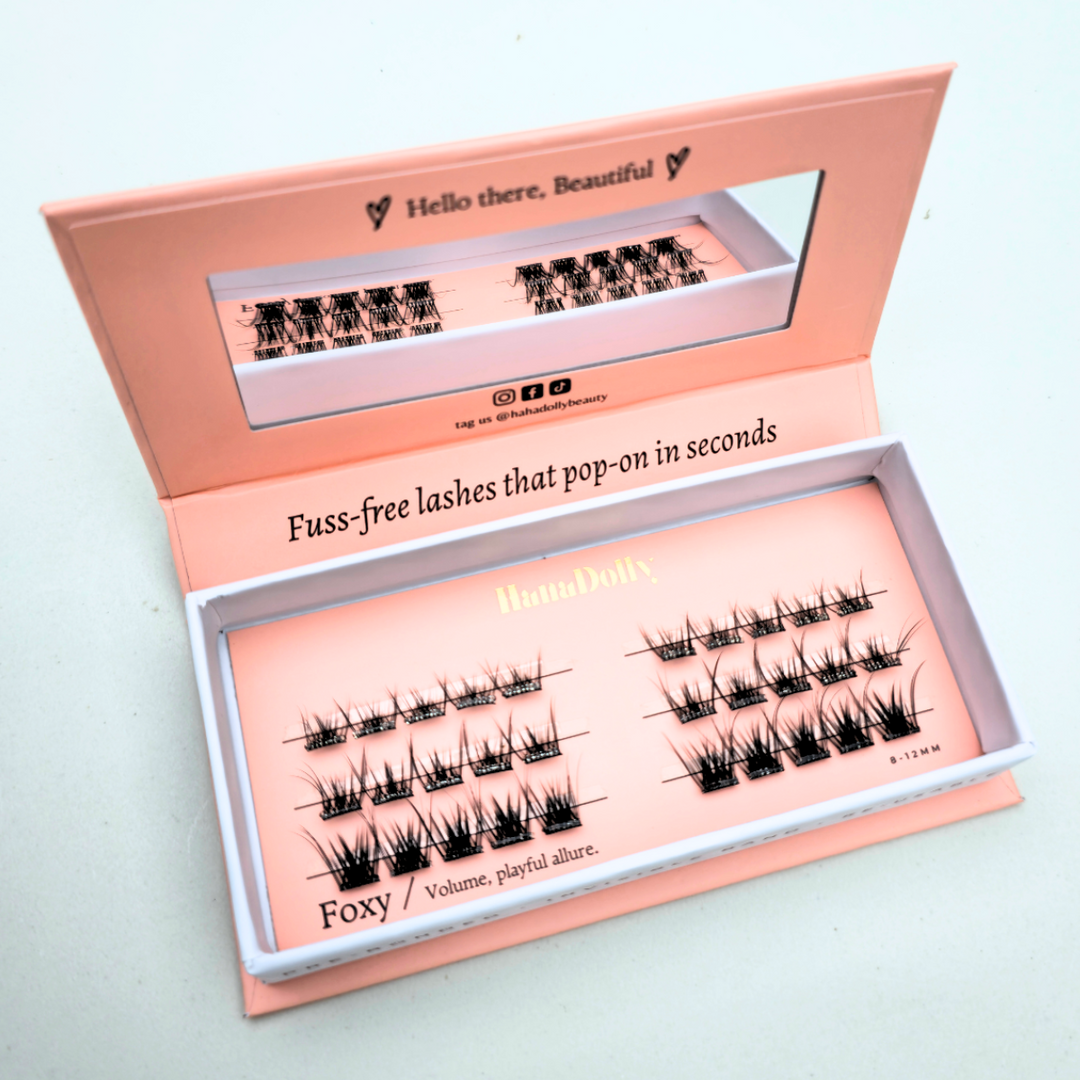 Angled flatlay of HanaDolly FOXY press-on lashes in an open pink box, showing individual lash clusters for easy application.