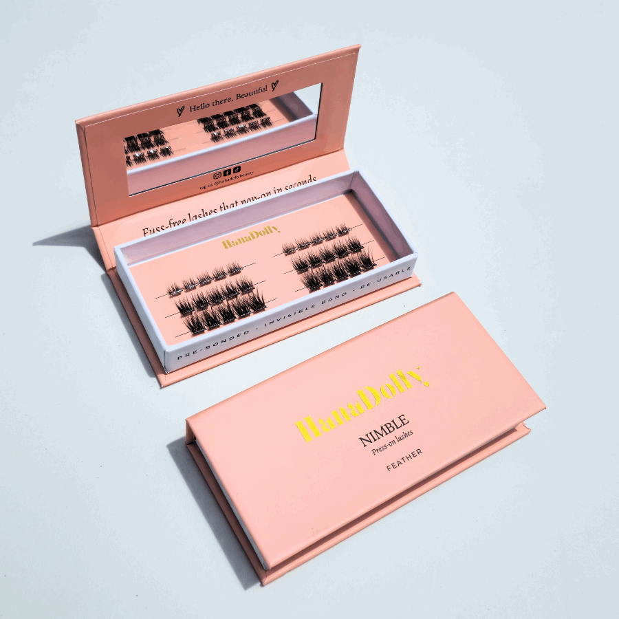 Flatlay of HanaDolly's Feather press-on lashes in an open pink HanaDolly box, showcasing reusable lashes with pre-bonded adhesive.