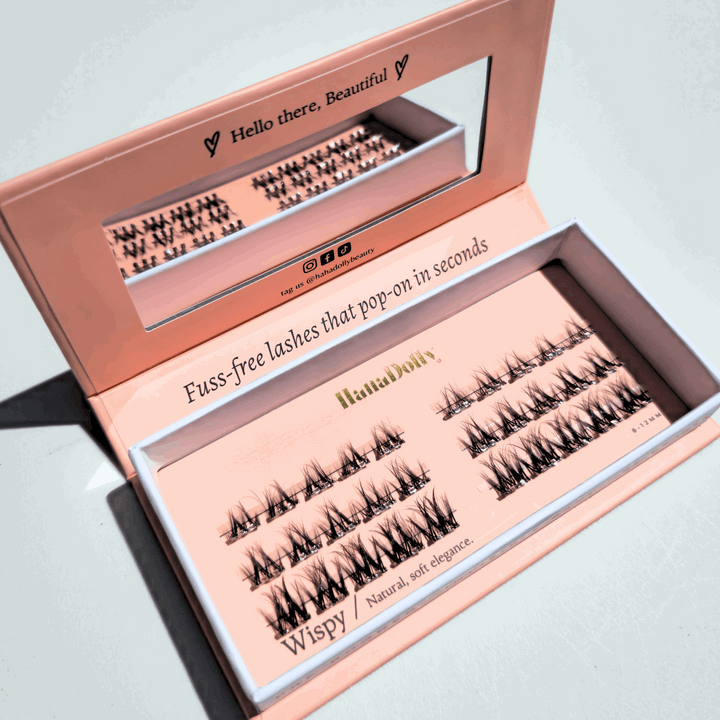 Angled flatlay of HanaDolly Wispy press-on lashes in an open pink box, showing individual lash clusters for easy application.